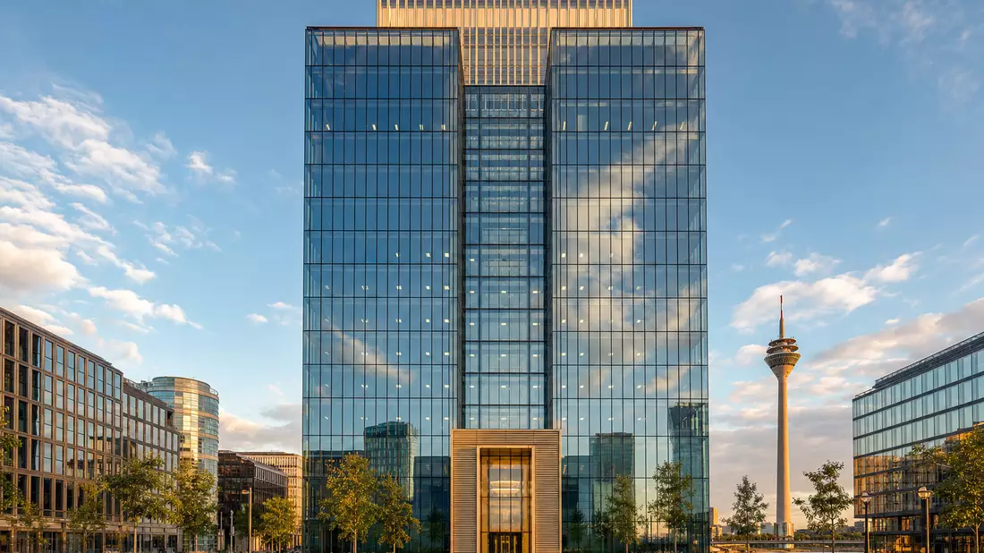 Moderner Glas-Büroturm in Düsseldorf mit Rheinturm im Hintergrund, goldene Stunde