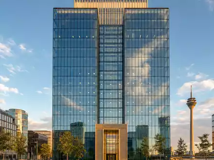 Professionelle Architekturfotografie eines modernen Glas-Stahl-Büroturms am Düsseldorfer Rheinufer mit dem Rheinturm im Hintergrund – verweist auf den Hauptsitz der Henkel AG & Co. KGaA (ISIN DE0006048432) in Düsseldorf, Deutschland - Foto: THN