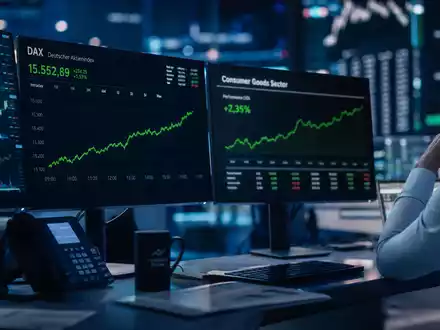 Stimmungsvolles Börsen-Editorial-Foto eines Traders vor mehreren Monitoren mit DAX-Chart und Consumer-Goods-Sektor-Index – illustriert die Kapitalmarktpräsenz der Henkel AG & Co. KGaA (ISIN DE0006048432) als börsennotiertes DAX-Unternehmen im deutschen Leitindex - Foto: THN