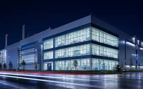 Architektonisches Nachtfoto eines modernen Halbleiterwerks mit leuchtenden Reinraumfenstern – vergleichbar mit den Produktionsstandorten von Infineon Technologies AG (ISIN DE0006231004) in der Region München und weltweit - Foto: THN