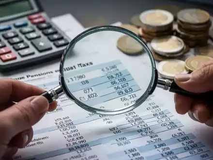 Eine Hand hält eine Lupe über ein Finanzdokument mit Renten- und Steuerzahlen, im Hintergrund ein Taschenrechner und Euro-Münzen. - Foto: über boerse-global.de