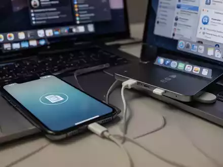 Ein iPhone, das per USB-C-Kabel mit einem MacBook Pro verbunden ist, zeigt ein Dateiübertragungssymbol auf dem Bildschirm. - Foto: über boerse-global.de