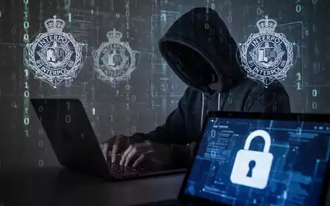 Ein verschatteter Hacker in Kapuzenjacke tippt auf einem Laptop, umgeben von digitalen Interpol-Logos und Binärcode. - Foto: über boerse-global.de