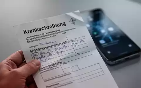 Eine Hand hält eine ärztliche Krankschreibung aus Papier, im Hintergrund verschwommen ein Smartphone, das die Abschaffung der telefonischen Krankschreibung symbolisiert. - Foto: über boerse-global.de