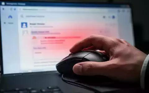Nahaufnahme einer Hand, die eine Computermaus hält, mit unscharfem Bildschirm im Hintergrund, der eine E-Mail-Oberfläche und eine rote Fehlerüberlagerung zeigt. - Foto: über boerse-global.de