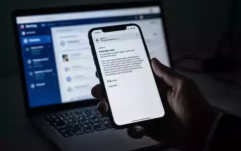Eine Hand hält ein Smartphone mit einer Phishing-E-Mail, im Hintergrund verschwommen ein Laptop mit Banking-Apps. - Foto: über boerse-global.de
