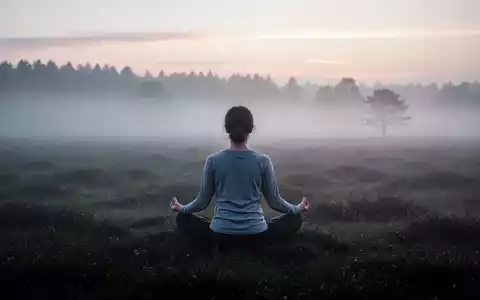Eine Person meditiert im Morgennebel eines Moores, umgeben von ruhiger Natur. Sonnenlicht bricht durch den Nebel. - Foto: über boerse-global.de
