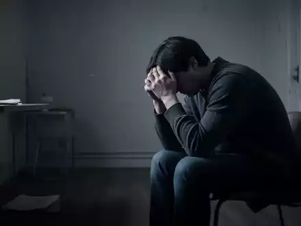 Eine Person sitzt allein in einem spärlich beleuchteten Raum, den Kopf in den Händen, Ausdruck von Stress und Isolation. - Foto: über boerse-global.de