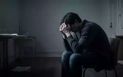 Eine Person sitzt allein in einem spärlich beleuchteten Raum, den Kopf in den Händen, Ausdruck von Stress und Isolation. - Foto: über boerse-global.de