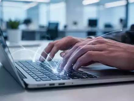 Nahaufnahme von Händen, die auf einer Laptop-Tastatur tippen, mit leuchtenden Linien, die Textvorschläge auf dem Bildschirm andeuten. - Foto: über boerse-global.de