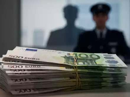 Ein Stapel Euro-Banknoten mit einer verschwommenen Silhouette eines Beamten im Hintergrund, symbolisiert Gehaltserhöhungen und Staatsausgaben. - Foto: über boerse-global.de