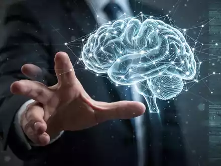Eine menschliche Hand greift nach einem leuchtenden, abstrakten digitalen Gehirnnetzwerk, das die Steuerung und Regulierung künstlicher Intelligenz symbolisiert. - Foto: über boerse-global.de
