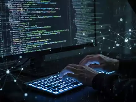 Hackerhände tippen auf Tastatur, Codezeilen auf Bildschirm, symbolisieren Cyberangriff. - Foto: über boerse-global.de