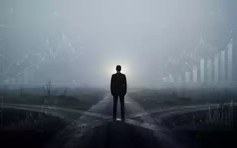 Eine einzelne, silhouettierte Figur steht an einer nebligen Weggabelung und blickt auf ein schwaches Licht am Horizont. - Foto: über boerse-global.de