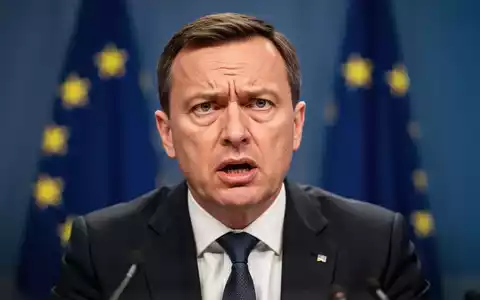 EU-Haushaltskommissar Piotr Serafin spricht auf einer Pressekonferenz, mit ernstem Gesichtsausdruck vor verschwommener EU-Flagge. - Foto: über boerse-global.de