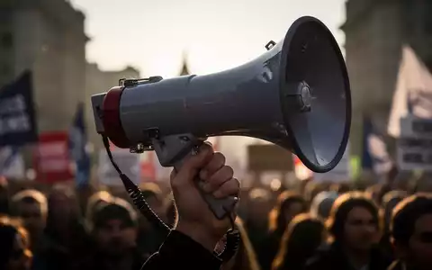 Nahaufnahme einer Hand, die ein Megafon hält, symbolisiert die Stimme der Gewerkschaften bei Protesten gegen Regierungspolitik. - Foto: über boerse-global.de
