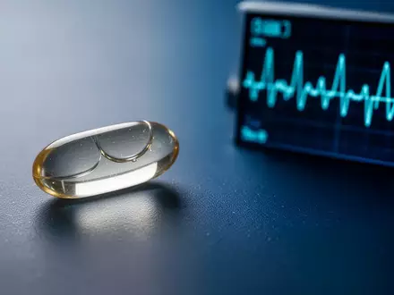 Eine Nahaufnahme einer silbernen Fischölkapsel neben einem unscharfen Herzmonitor auf einem dunklen, medizinischen Hintergrund. - Foto: über boerse-global.de