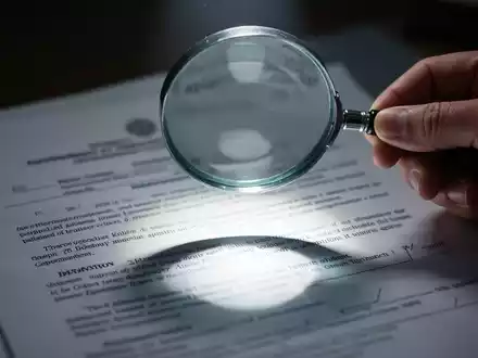 Eine Hand hält eine Lupe über ein verschwommenes Regierungsdokument, das Transparenz und staatliche Informationen symbolisiert. - Foto: über boerse-global.de