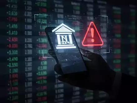 Eine Hand hält ein Smartphone, das ein Banklogo und ein Warnzeichen auf einen dunklen Hintergrund mit Finanzdaten projiziert. - Foto: über boerse-global.de