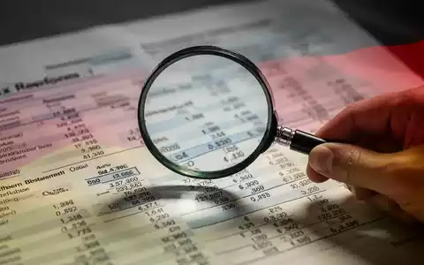 Eine Hand hält eine Lupe über ein komplexes Finanzdokument mit verschwommenem Text und Zahlen, das Steuerausfälle symbolisiert. - Foto: über boerse-global.de