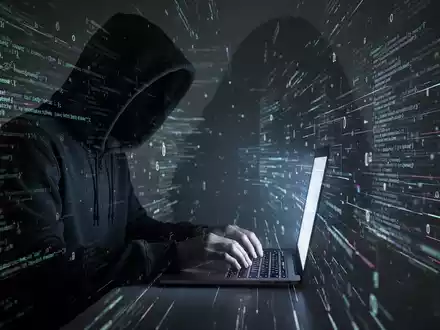 Person in dunklem Hoodie tippt auf Laptop mit leuchtendem Code, symbolisiert Datenschutzlücke in Apples 'Hide My Email'-Funktion. - Foto: über boerse-global.de