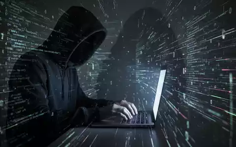 Person in dunklem Hoodie tippt auf Laptop mit leuchtendem Code, symbolisiert Datenschutzlücke in Apples 'Hide My Email'-Funktion. - Foto: über boerse-global.de