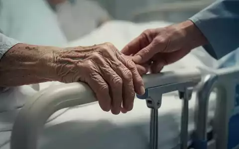 Eine ältere Hand ruht auf einem Krankenhausbettgeländer, eine andere Hand berührt sie sanft zur Beruhigung. - Foto: über boerse-global.de