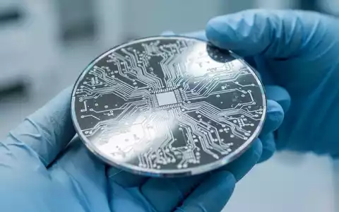 Nahaufnahme eines reflektierenden Siliziumwafers mit feinen Schaltkreismustern, gehalten von einer behandschuhten Hand im Reinraum. - Foto: über boerse-global.de