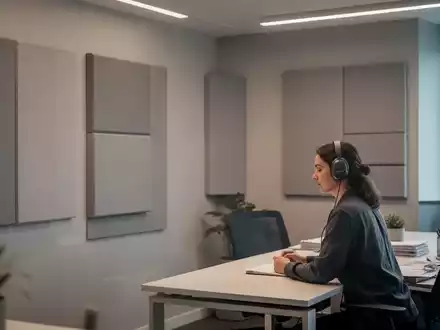 Ein ruhiges, modernes Bürozimmer mit gedämpftem Licht, schallabsorbierenden Paneelen an den Wänden und einer Person mit Kopfhörern am Schreibtisch. - Foto: über boerse-global.de