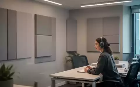 Ein ruhiges, modernes Bürozimmer mit gedämpftem Licht, schallabsorbierenden Paneelen an den Wänden und einer Person mit Kopfhörern am Schreibtisch. - Foto: über boerse-global.de