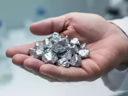 Nahaufnahme einer Hand, die glänzende Zinkmineralfragmente hält, mit weichgezeichnetem Hintergrund. - Foto: über boerse-global.de