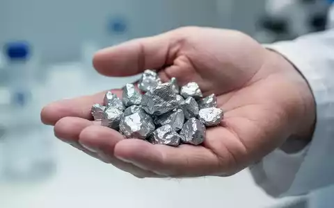 Nahaufnahme einer Hand, die glänzende Zinkmineralfragmente hält, mit weichgezeichnetem Hintergrund. - Foto: über boerse-global.de