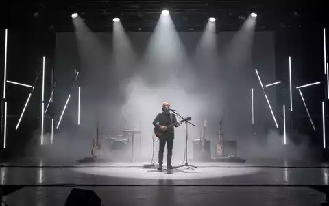 Ein einzelner Musiker auf einer spärlich beleuchteten Bühne, umgeben von Nebel, symbolisiert Minimalismus in der Musik. - Foto: über boerse-global.de