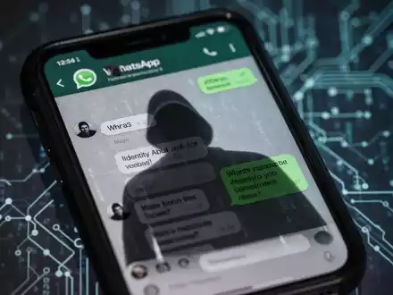Ein Smartphone-Bildschirm zeigt eine WhatsApp-Konversation mit einer bedrohlichen, verschwommenen Reflexion, die Cyberkriminalität symbolisiert. - Foto: über boerse-global.de