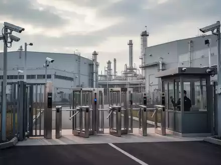 Eine moderne Zugangskontrolle mit Schranken, Kameras und einem Wachhäuschen an einem großen Industriepark. - Foto: über boerse-global.de