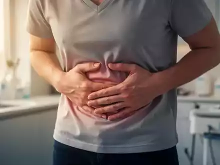 Eine Person hält sich den Bauch, um Beschwerden zu lindern, mit sanftem Licht, das durch ein Fenster fällt. - Foto: über boerse-global.de
