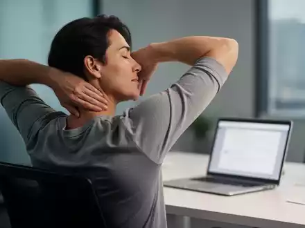 Eine Person dehnt sanft Nacken und Schultern an einem Büroschreibtisch, während ein Laptop im Hintergrund unscharf ist. - Foto: über boerse-global.de