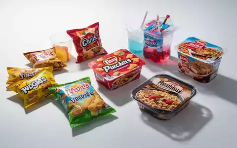 Nahaufnahme von ultra-verarbeiteten Lebensmitteln wie bunten Snacks und Zuckergetränken auf weißem Hintergrund, die künstliche Natur hervorhebend. - Foto: über boerse-global.de