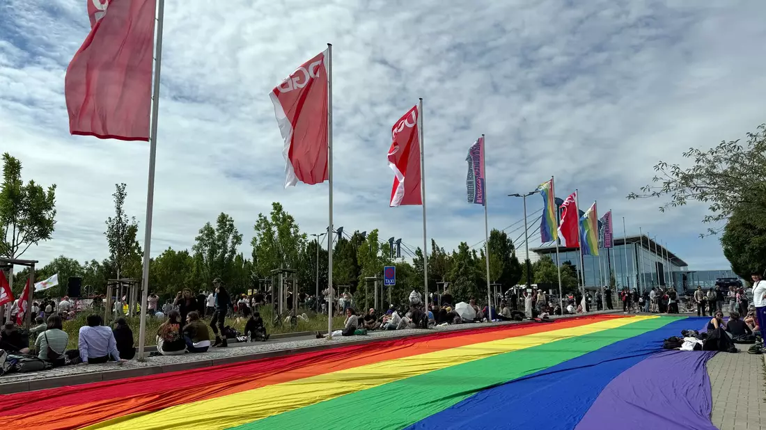 Eine übergroße Regenbogenfahne liegt ausgebreitet neben einer Kundgebung des DGB in Erfurt - Bild: Sarah Knorr/dpa