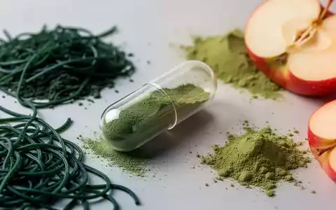 Eine transparente Kapsel mit grünem Pulver, umgeben von Spirulina, Matcha und Apfelessig-Extrakt, auf hellem Untergrund. - Foto: über boerse-global.de