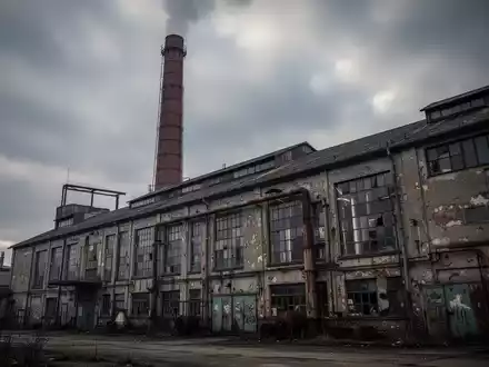 Ein verwittertes, industrielles Brauereigebäude mit einem markanten Schornstein unter einem dramatischen, bedeckten Himmel. - Foto: über boerse-global.de