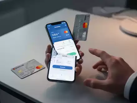 Eine Hand hält ein Smartphone mit Zahlungs-App, daneben eine deutsche Girocard auf einem modernen Tisch – Symbol für digitales Bezahlen. - Foto: über boerse-global.de
