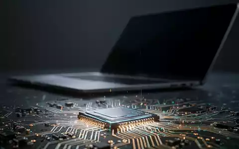 Nahaufnahme eines leuchtenden Mikrochips mit feinen Schaltkreisen, im unscharfen Hintergrund dezent ein Laptop angedeutet. - Foto: über boerse-global.de