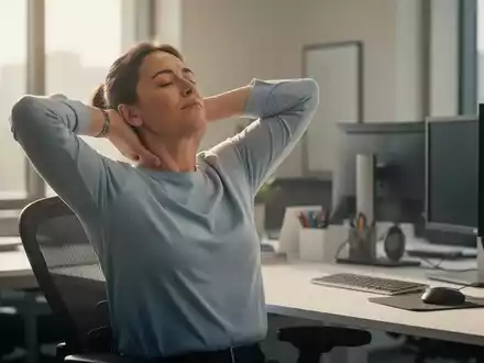 Eine Person dehnt sanft Nacken und Schultern an einem ergonomischen Büroschreibtisch, um Schmerzen zu lindern. - Foto: über boerse-global.de