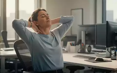 Eine Person dehnt sanft Nacken und Schultern an einem ergonomischen Büroschreibtisch, um Schmerzen zu lindern. - Foto: über boerse-global.de