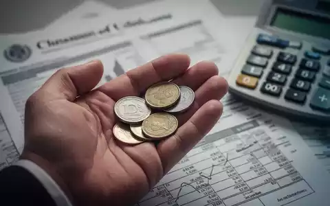Nahaufnahme einer Hand, die Münzen hält, im Hintergrund unscharfe Finanzdokumente und ein Taschenrechner. - Foto: über boerse-global.de