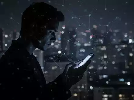Silhouette blickt auf Smartphone mit digitalem Netz-Overlay vor verschwommener, dunkler Stadtlandschaft. - Foto: über boerse-global.de