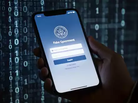 Nahaufnahme einer Hand, die ein Smartphone mit gefälschter Regierungs-Loginseite hält, unscharfer Binärcode-Hintergrund. - Foto: über boerse-global.de