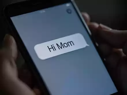 Nahaufnahme eines Smartphones, das eine betrügerische „Hi Mom“-Nachricht anzeigt. Hände halten das Telefon, im Hintergrund verschwommen. - Foto: über boerse-global.de