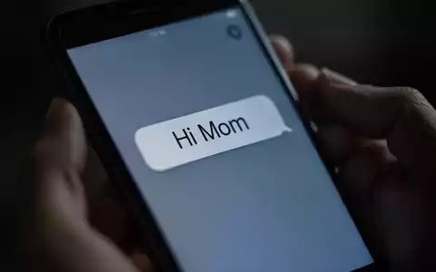 Nahaufnahme eines Smartphones, das eine betrügerische „Hi Mom“-Nachricht anzeigt. Hände halten das Telefon, im Hintergrund verschwommen. - Foto: über boerse-global.de